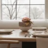 Textured vase with pink rose and gold leaf on a dining table, elegant floral display.