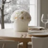 Cream-colored vase with white flowers on a dining table, elegant floral arrangement.
