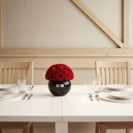 Black ceramic vase with red roses on a dining table, elegant floral arrangement.