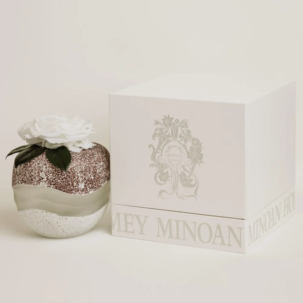 Elegant textured sphere candle with glittering white base topped with white rose and green leaves beside matching box