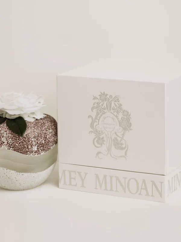 Elegant textured sphere candle with glittering white base topped with white rose and green leaves beside matching box