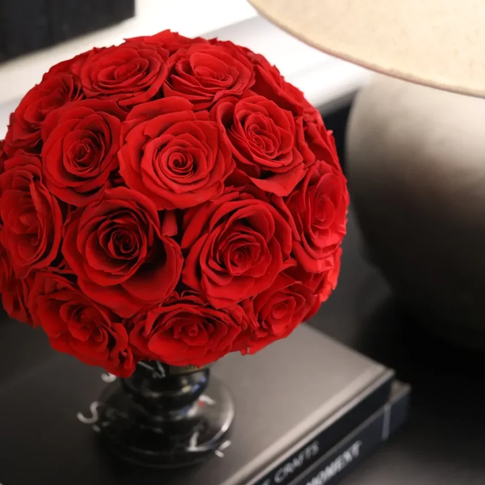 Vibrant red rose bouquet in glass vase atop stack of books with lampshade