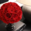Vibrant red rose bouquet in glass vase atop stack of books with lampshade