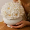 Asian woman in beige dress inhaling fragrance of white hydrangea bouquet in ceramic pot