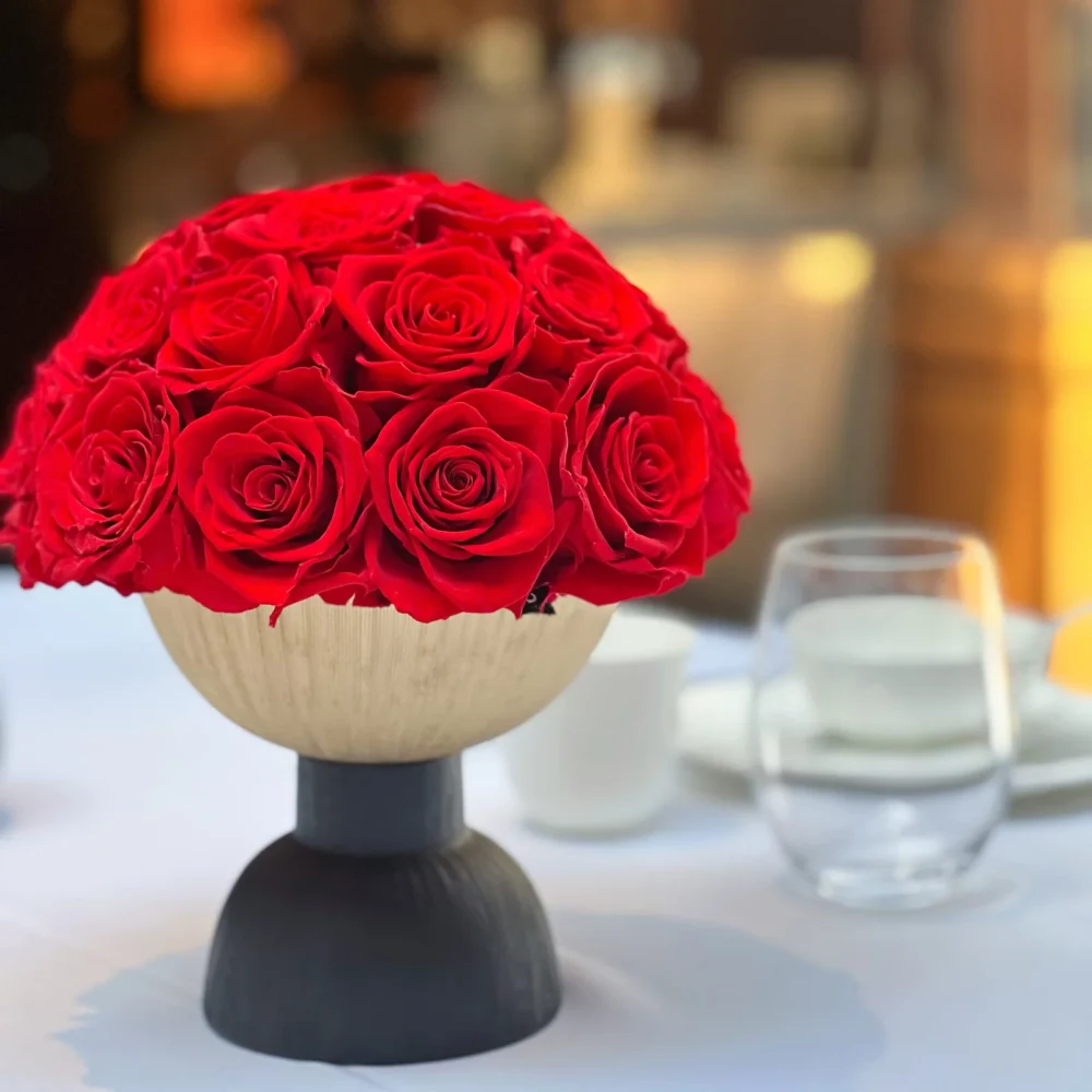 Light wood vase with black base holding red roses bouquet with wine glasses