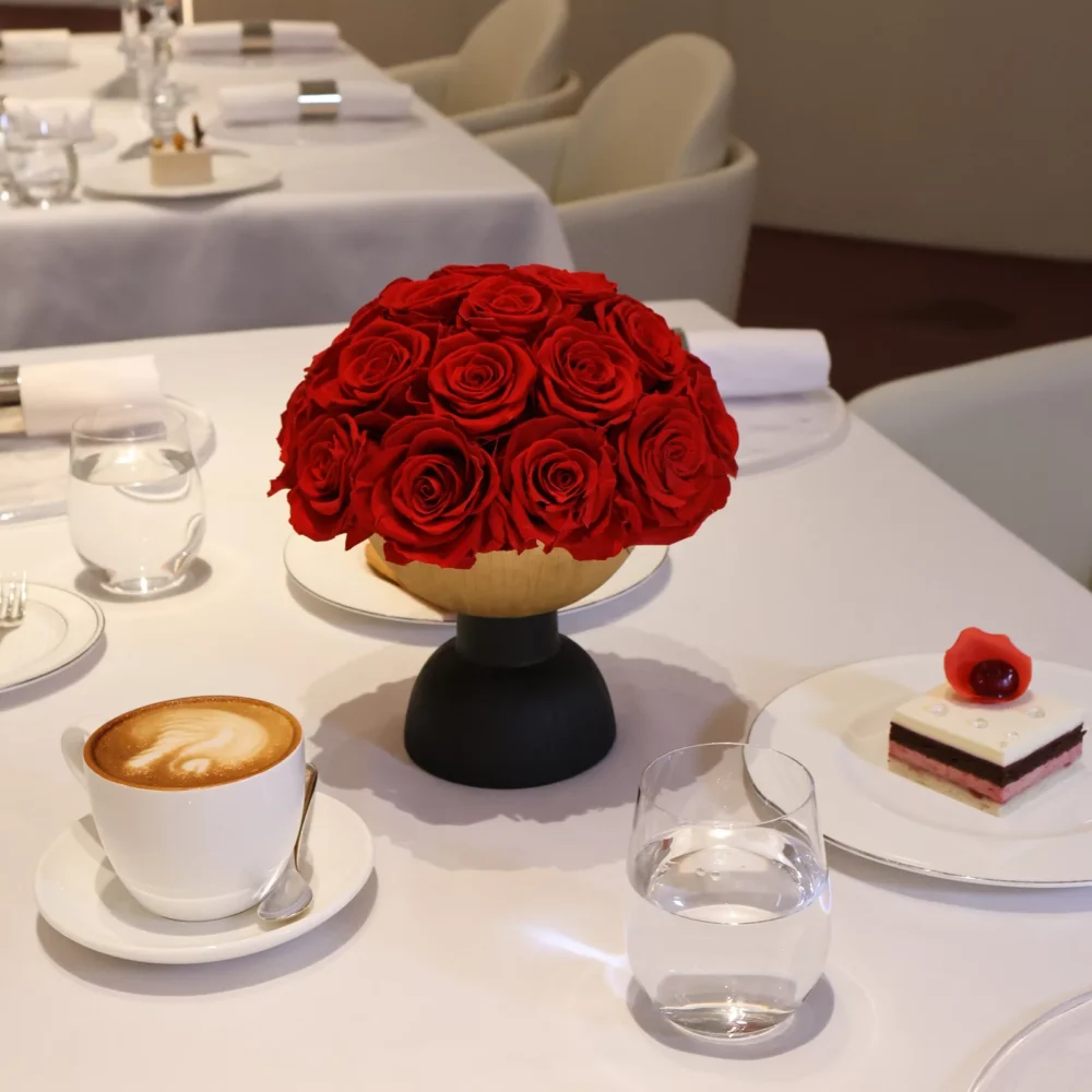 Formal dining table with black vase holding red roses and latte cup