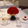 Formal dining table with black vase holding red roses and latte cup