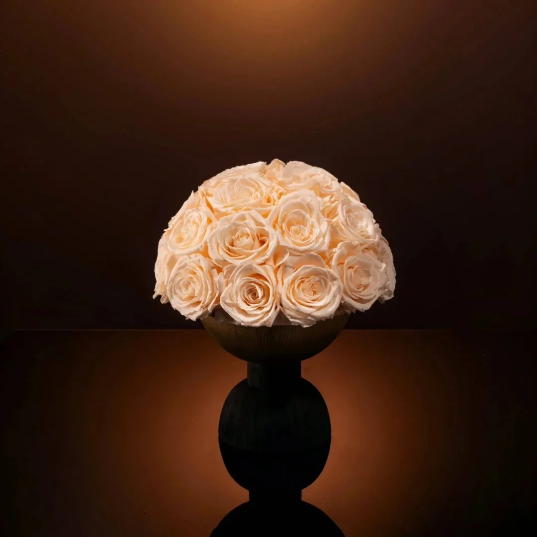 Cylindrical glass vase with lush cream roses on reflective black surface