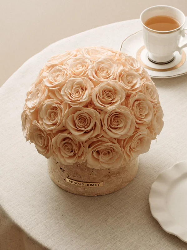 Round beige table with large pale peach rose bouquet and white porcelain cup with light brown beverage