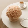 Round beige table with large pale peach rose bouquet and white porcelain cup with light brown beverage