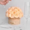 Cream spherical floral arrangement in beige vase with "MIDAS HONEY" label as hand pours water