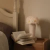 Serene bedroom with wooden nightstand holding open book and vase of delicate white flowers against cream wall