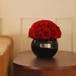 Round dark wooden table with black vase of red roses and "Bella Donna" silver tag