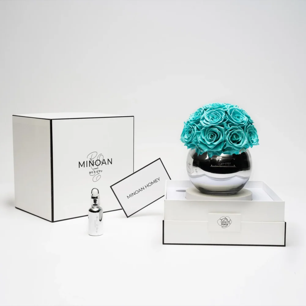 Minimalist elegant setup with clear glass vase of turquoise artificial roses beside "Minoa by Maison Margiela" box