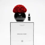 Minimalist elegant setup featuring black spherical glass vase with red roses on "MINDAN HONEY" labeled box
