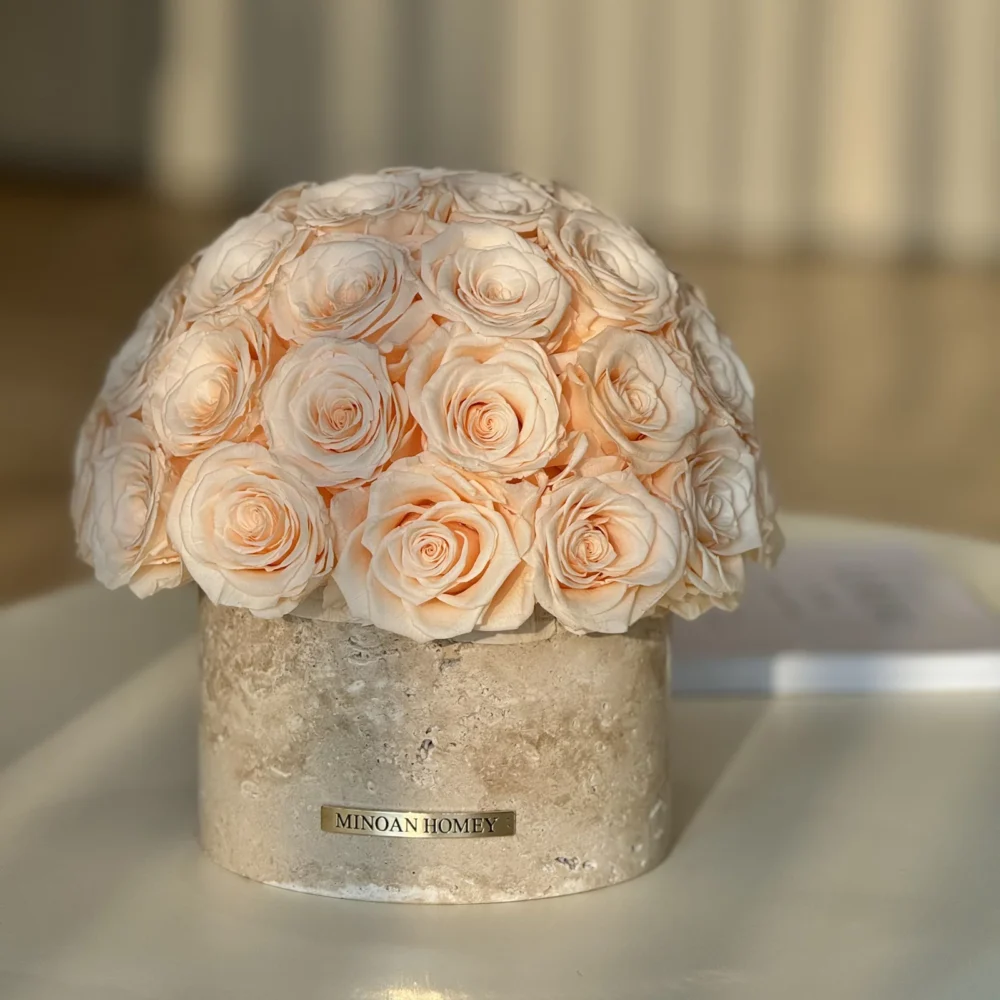 Round beige ceramic vase labeled "MIRAX HOMME" with pale peach rose bouquet on white surface