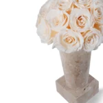 White rose bouquet in beige marble square-based vase with smooth polished surface and natural veining against white background