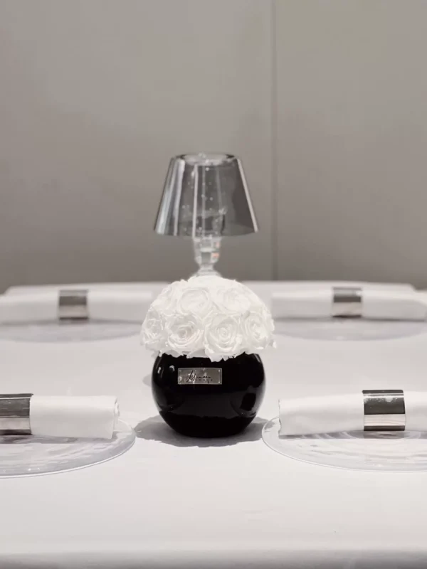 Minimalist dining table setting with small black vase containing white floral arrangement and silver-rimmed plates