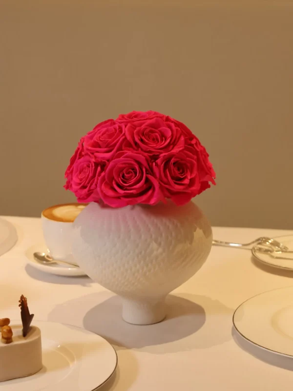 Elegant white ceramic vase with pink roses bouquet surrounded by ornate desserts