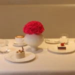 Modern dining setup with white ceramic vase containing pink rose and desserts