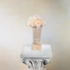 Pale peach vase with cream roses on white marble column. Classical floral designs and beige wall create a floral-themed sophisticated display.