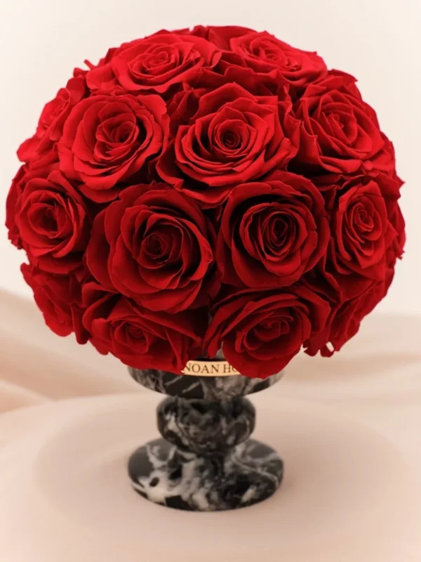 Lush bouquet of red roses in marble-effect vase with "TOMMIL" gold label on cream fabric