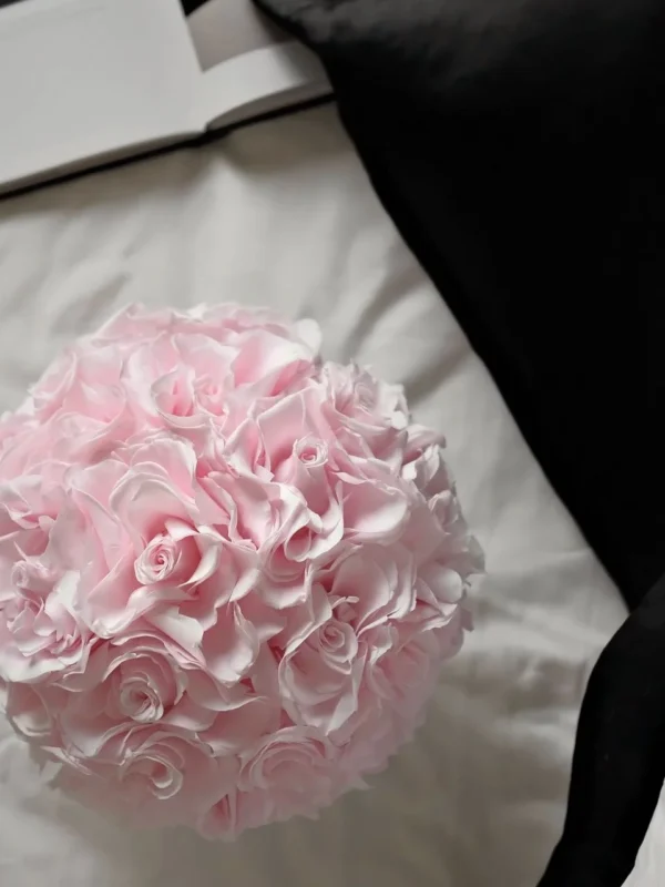 Close-up of light pink ruffled flower bouquet on white bed sheet with black fabric