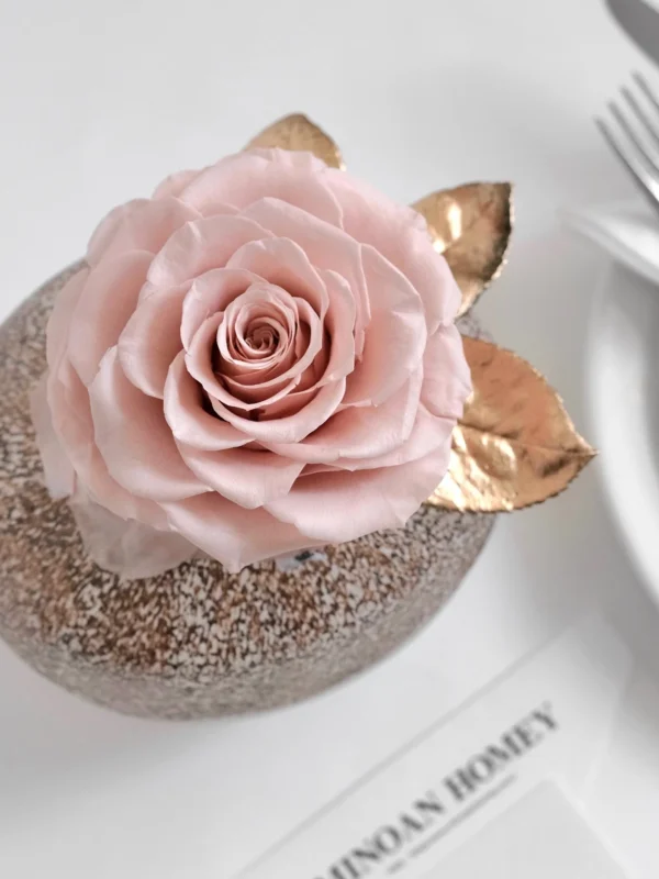 Close-up of pink rose cake topper with golden leaves on glittery bronze sphere base
