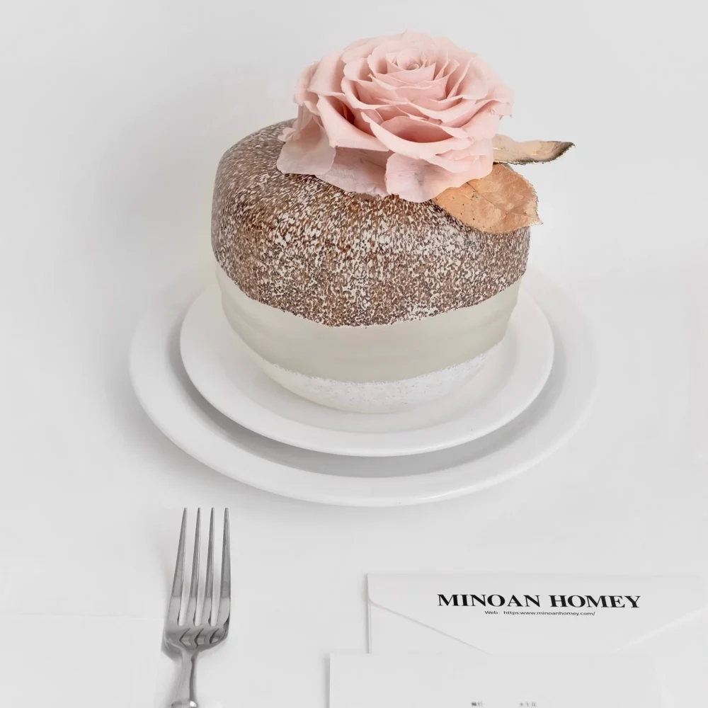 Two-tiered white and brown cake with pink rose and edible glitter on stand