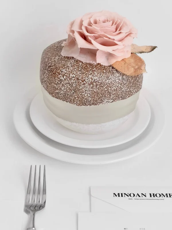Two-tiered white and brown cake with pink rose and edible glitter on stand