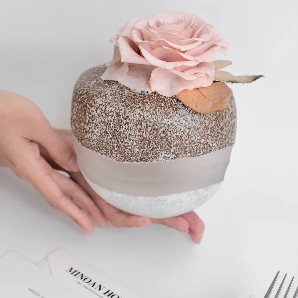 Small spherical jar with chia pudding and pink artificial rose on white surface