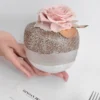 Small spherical jar with chia pudding and pink artificial rose on white surface