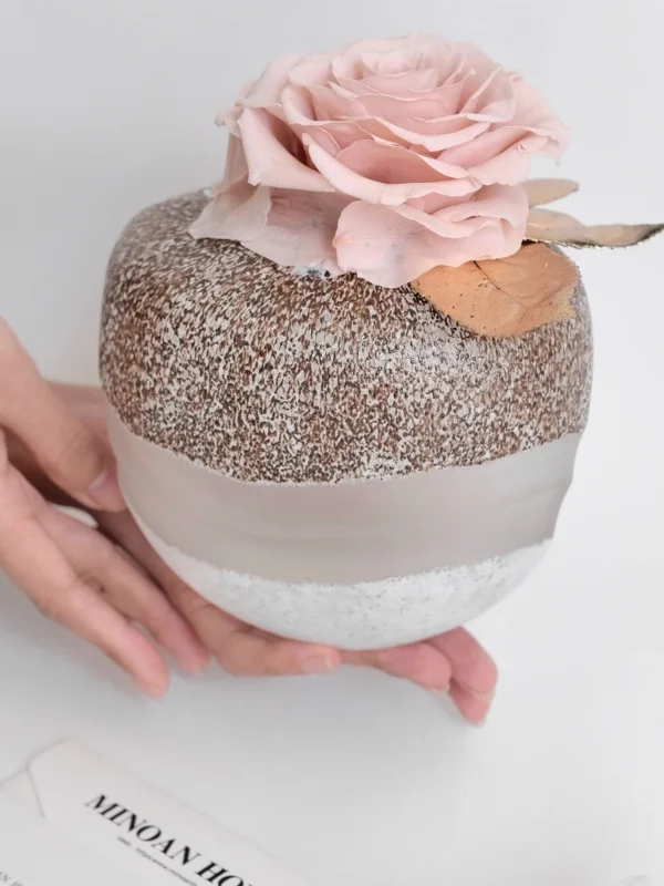 Small spherical jar with chia pudding and pink artificial rose on white surface