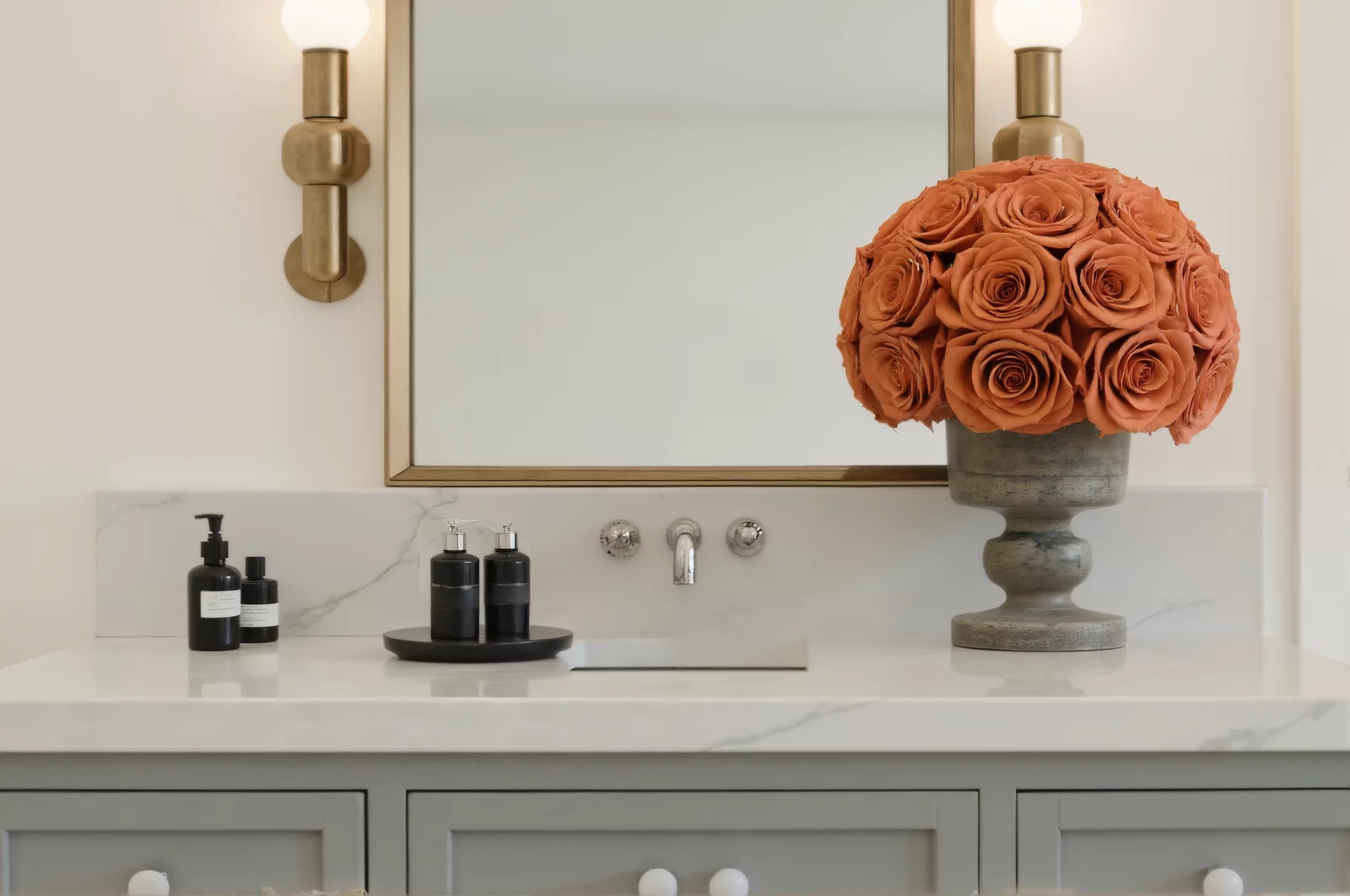 Coral-colored flower arrangement in a gray stone vase in a bathroom, modern floral display.