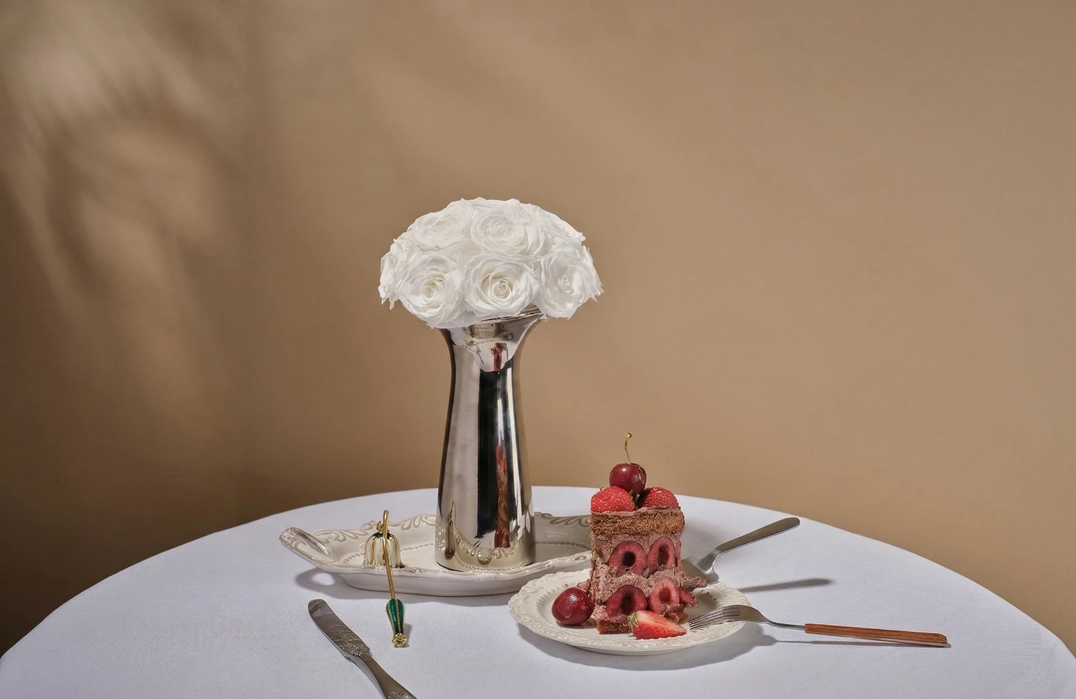 Metallic vase with white roses on a dining table, modern floral display.