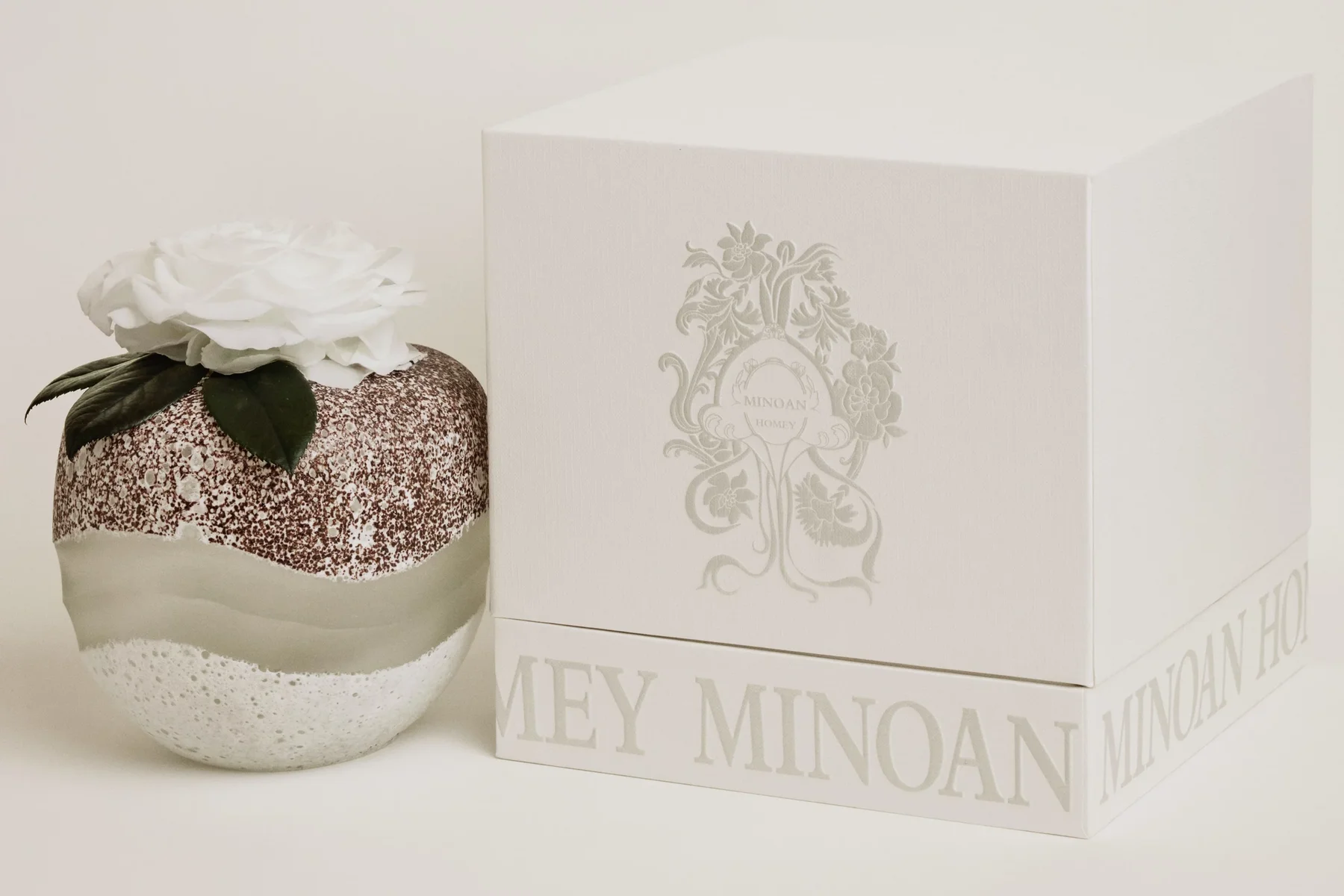 Elegant textured sphere candle with glittering white base topped with white rose and green leaves beside matching box