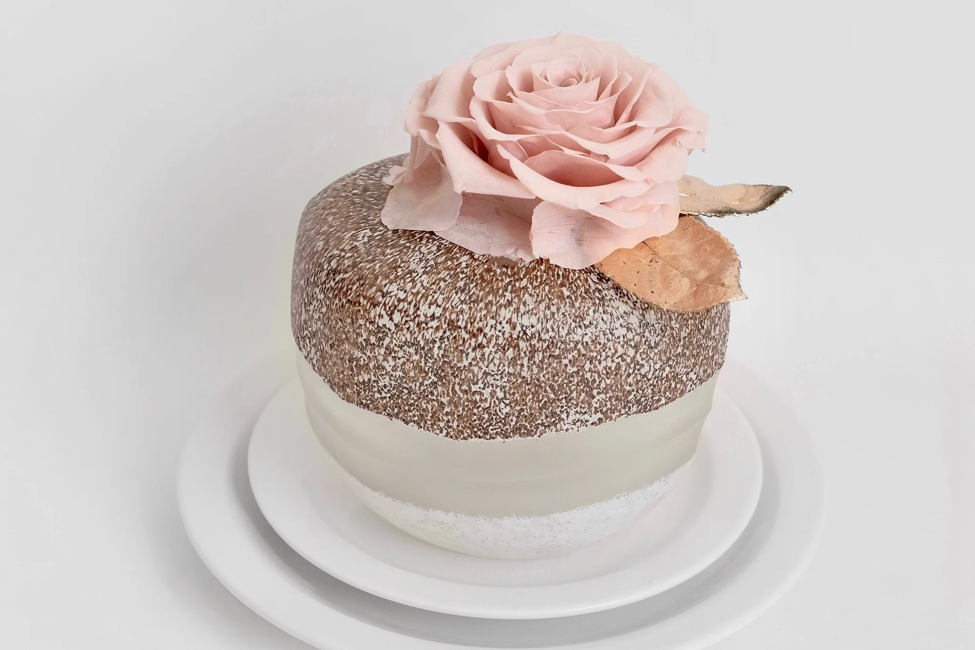 Two-tiered white and brown cake with pink rose and edible glitter on stand