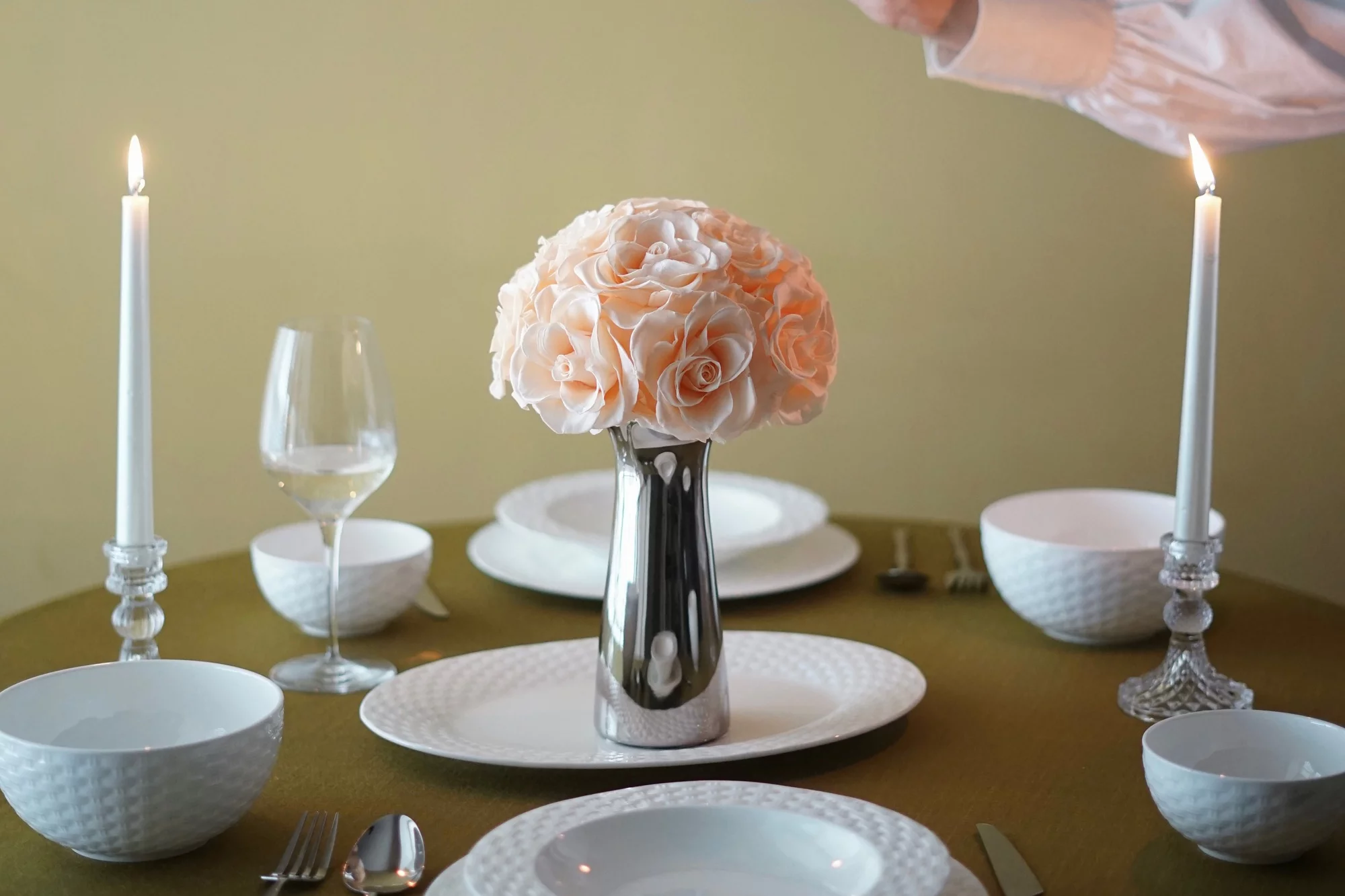 Elegantly set dining table with silver vase of peach roses and wine glass