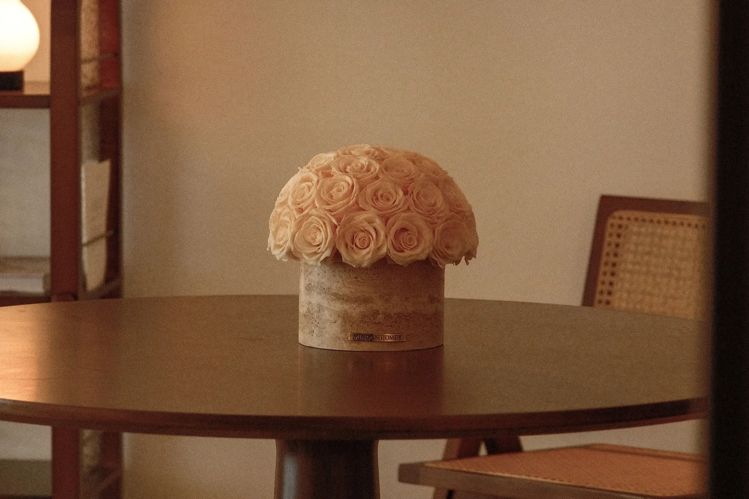 Minimalist cozy room with beige ceramic vase of pale pink roses on wooden table and wicker chair