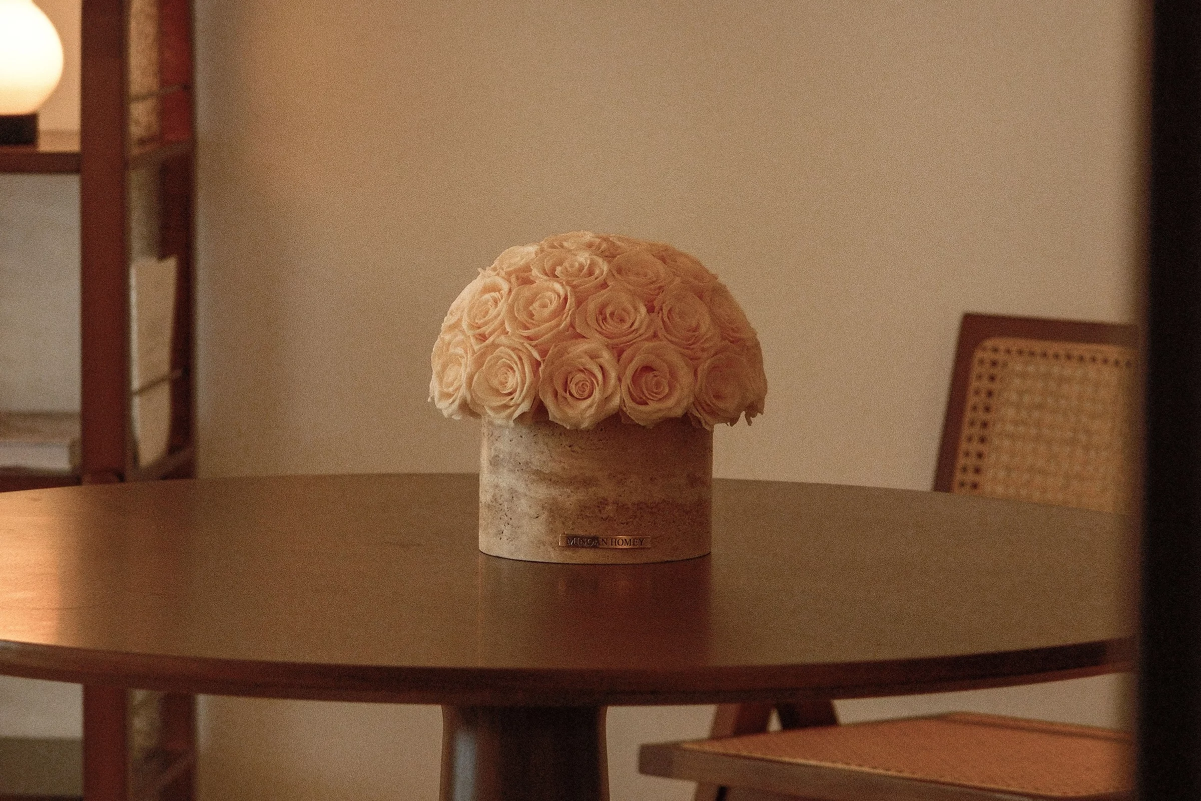 Minimalist cozy room with beige ceramic vase of pale pink roses on wooden table and wicker chair