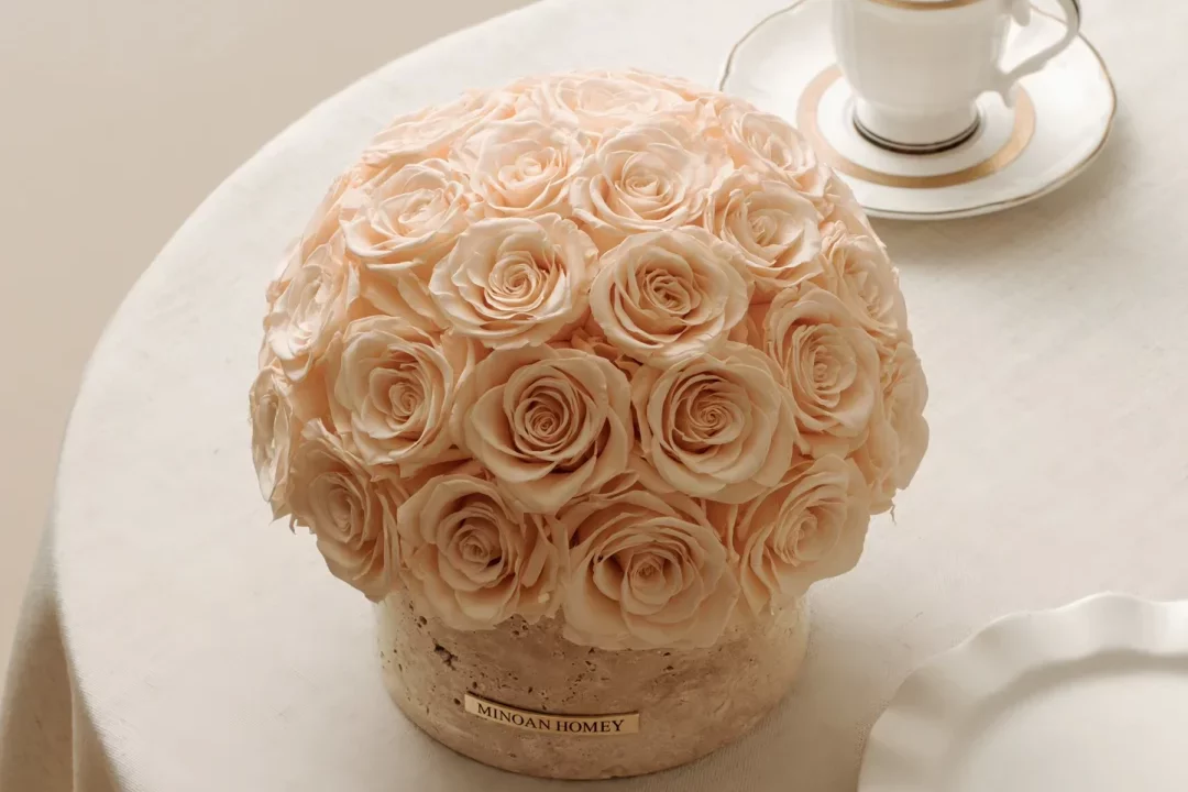Round white table with pale pink rose bouquet on beige ceramic base and white teacup with saucer
