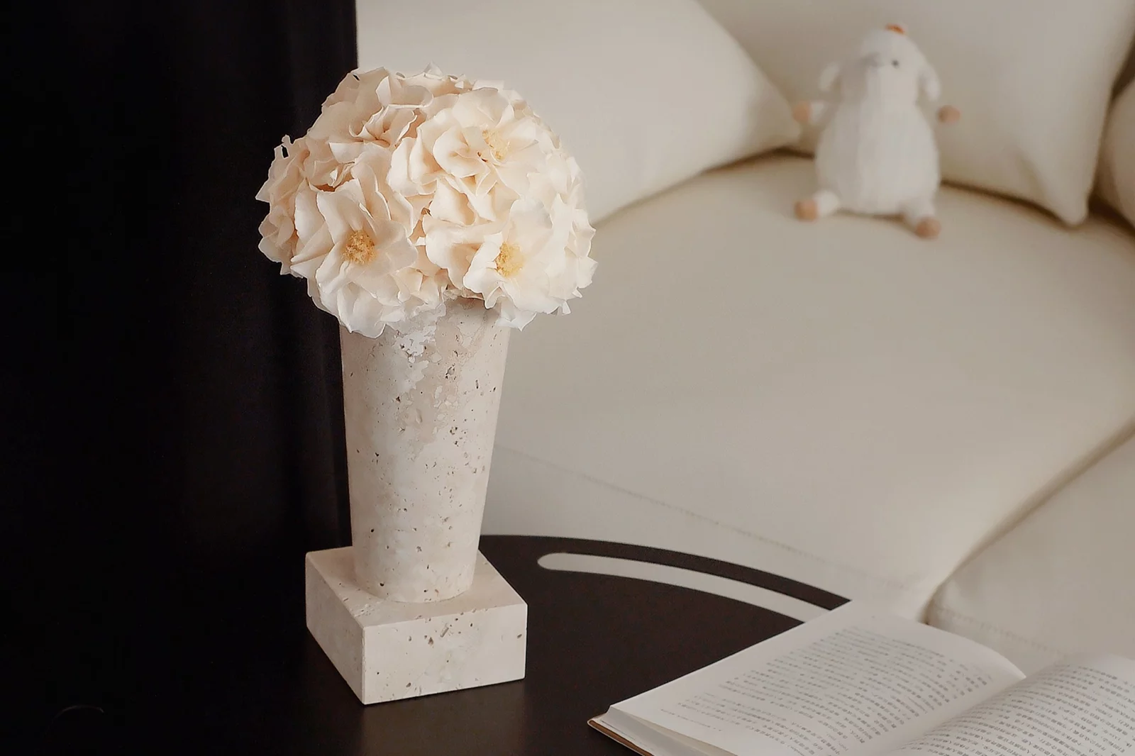 Serene living room with black coffee table holding beige vase of white floral arrangements