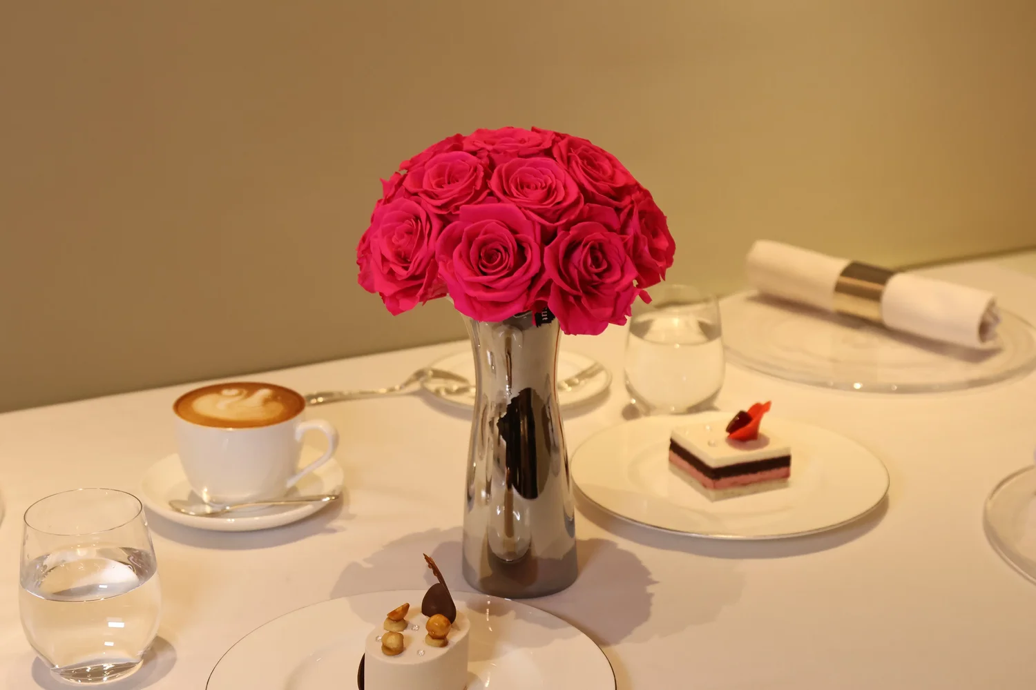 Minimalist table setting with pink roses bouquet in vase beside coffee cup and cake