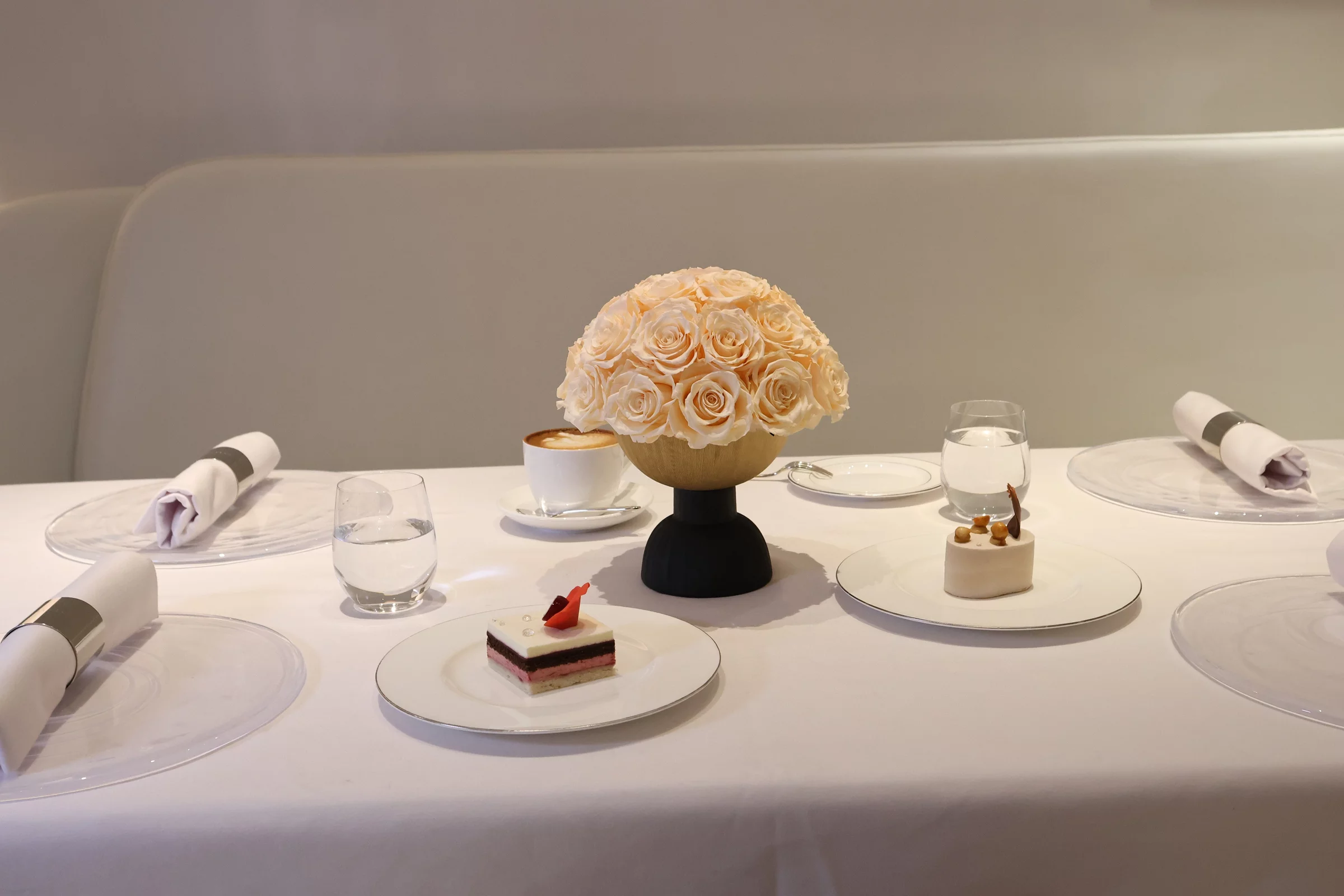 Beige ceramic vase with cream roses bouquet beside layered cake