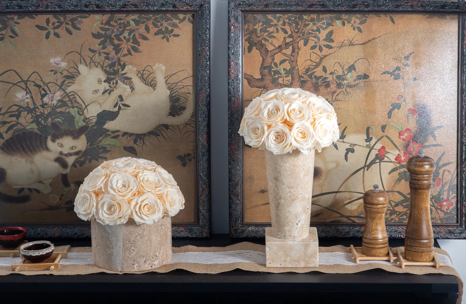 Ornate ceramic vases with cream floral arrangements on dark wood surface alongside Japanese ukiyo-e prints and wooden pepper mills