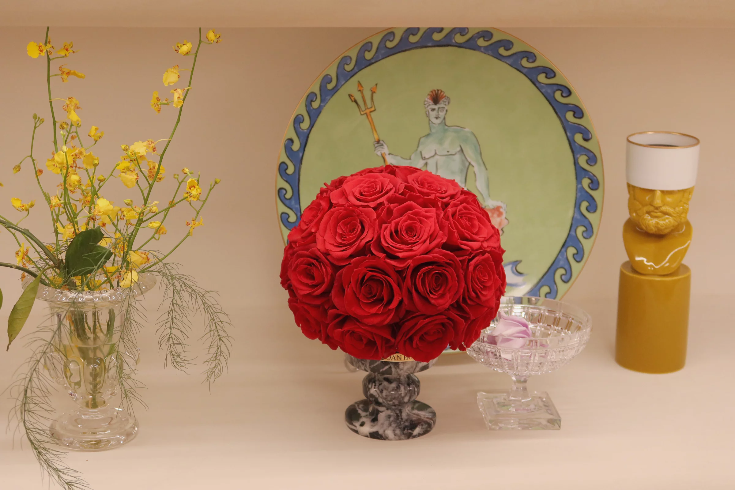 Serene minimalistic tabletop with glass vase of yellow flowers and vibrant red roses on black marble pedestal