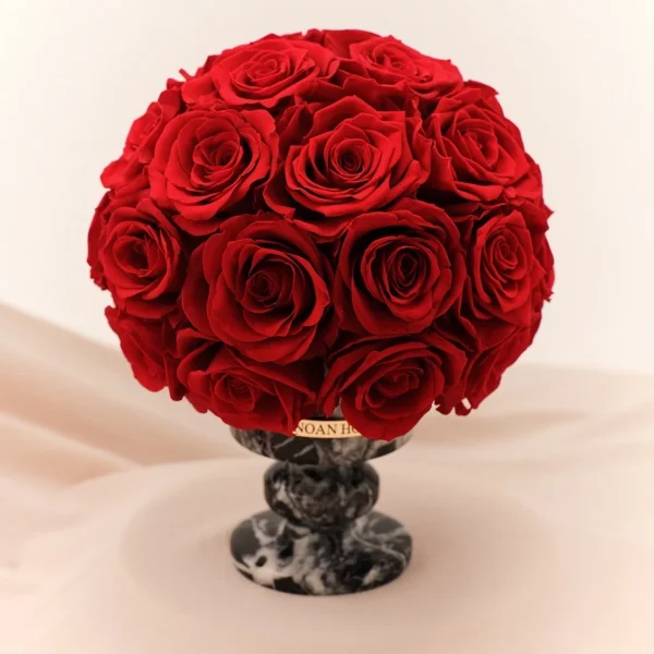 Lush bouquet of red roses in marble-effect vase with "TOMMIL" gold label on cream fabric
