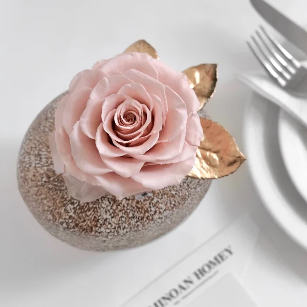 Close-up of pink rose cake topper with golden leaves on glittery bronze sphere base