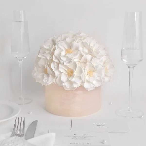 Tall pale pink cylindrical vase with white ruffled flowers and champagne flutes