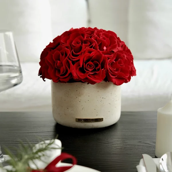Small beige vase with red roses on wooden table